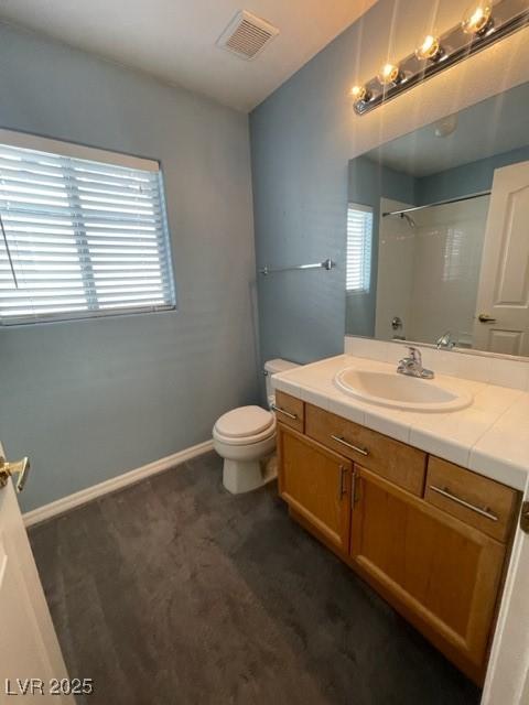 bathroom with toilet, vanity, visible vents, baseboards, and walk in shower