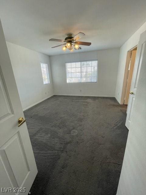 unfurnished room featuring ceiling fan, dark carpet, and baseboards