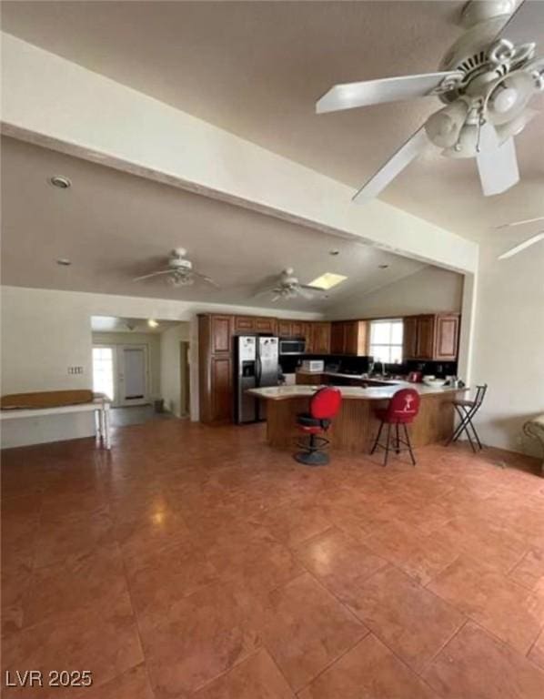 kitchen with a peninsula, a ceiling fan, a kitchen breakfast bar, vaulted ceiling, and appliances with stainless steel finishes