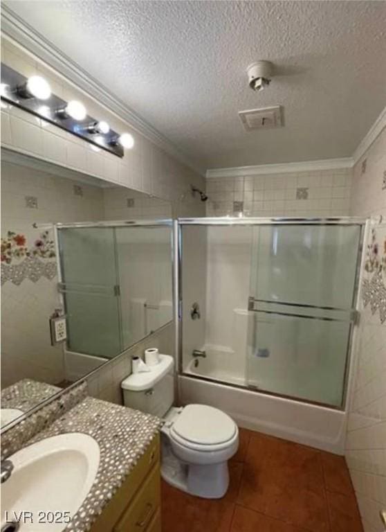 bathroom with a textured ceiling, shower / bath combination with glass door, toilet, and crown molding