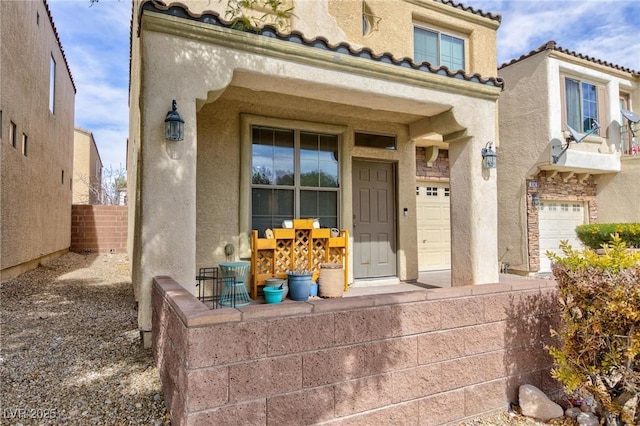 view of exterior entry featuring a garage, a tiled roof, and stucco siding