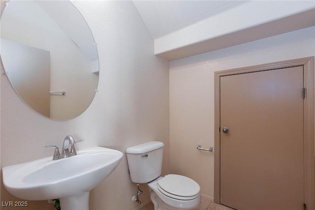 half bath with toilet, tile patterned flooring, baseboards, and a sink