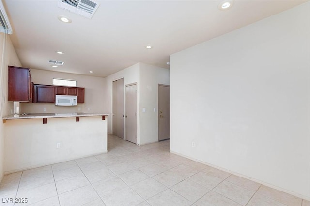 kitchen with visible vents, white microwave, a kitchen breakfast bar, a peninsula, and light countertops