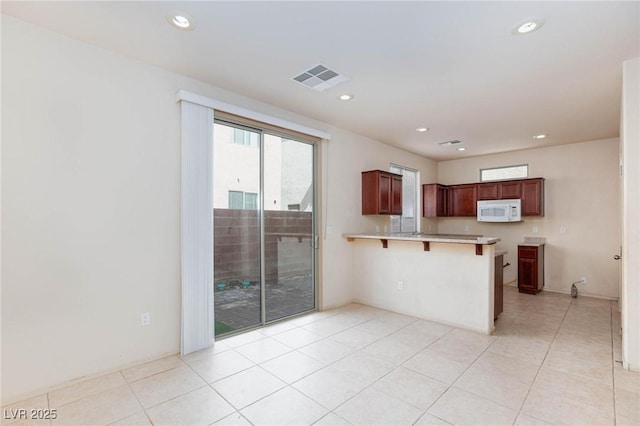 kitchen featuring visible vents, white microwave, a peninsula, light countertops, and a kitchen bar