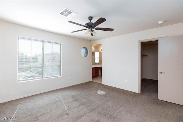 unfurnished bedroom with connected bathroom, carpet flooring, a ceiling fan, visible vents, and a walk in closet