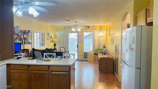 kitchen with brown cabinets, light countertops, a ceiling fan, open floor plan, and white appliances