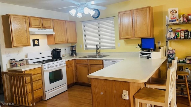 kitchen with under cabinet range hood, a peninsula, white appliances, a sink, and a kitchen breakfast bar