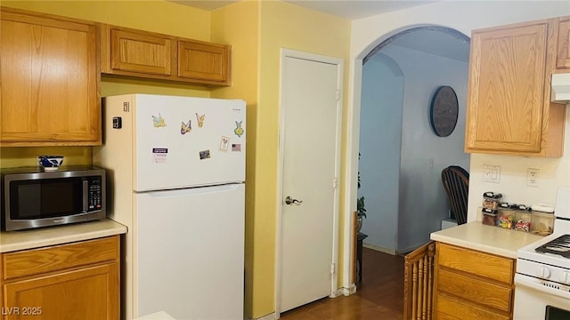 kitchen with arched walkways, under cabinet range hood, white appliances, light countertops, and dark wood finished floors