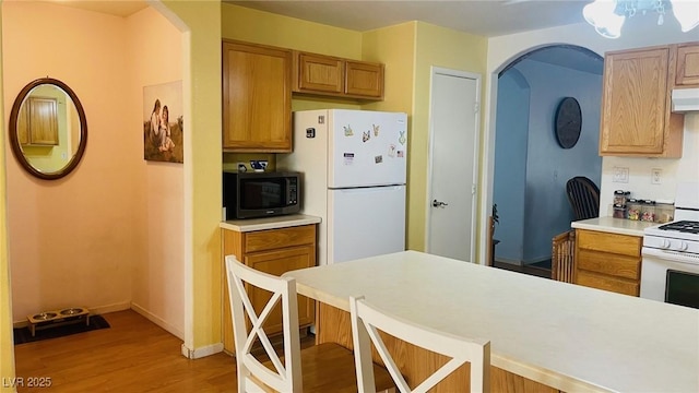 kitchen with white appliances, light wood finished floors, a breakfast bar area, light countertops, and ventilation hood