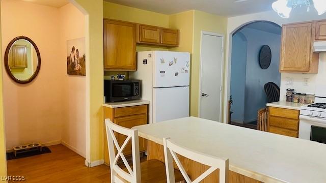 kitchen featuring light wood finished floors, light countertops, white appliances, under cabinet range hood, and a kitchen bar