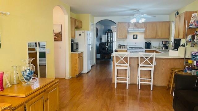 kitchen featuring arched walkways, under cabinet range hood, a peninsula, white appliances, and wood finished floors