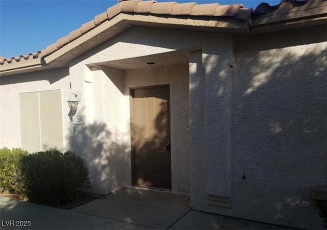 doorway to property with a patio, a tile roof, and stucco siding