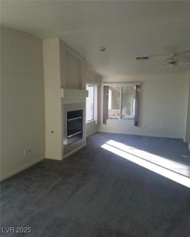 unfurnished living room featuring ceiling fan, dark carpet, a glass covered fireplace, and visible vents