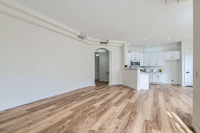 unfurnished living room with light wood-type flooring, visible vents, arched walkways, and baseboards