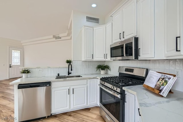 kitchen featuring visible vents, a sink, white cabinetry, stainless steel appliances, and light stone countertops