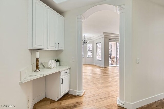 corridor featuring light wood-style flooring, baseboards, arched walkways, and ornate columns