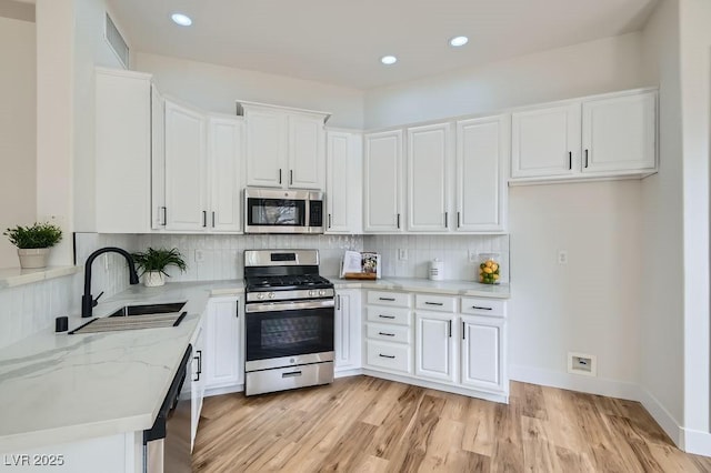 kitchen with light wood finished floors, a sink, white cabinets, appliances with stainless steel finishes, and tasteful backsplash