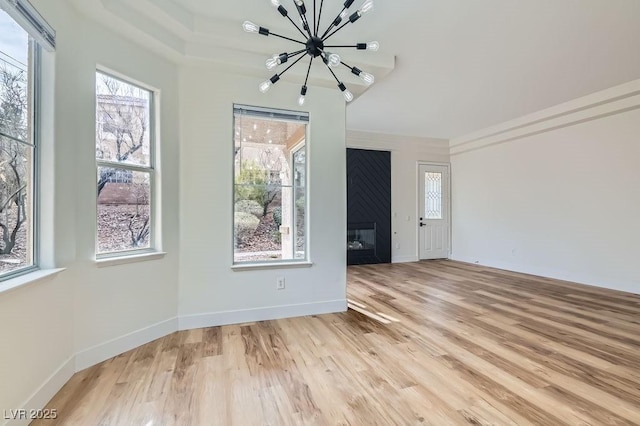 unfurnished room featuring an inviting chandelier, a fireplace, baseboards, and light wood finished floors