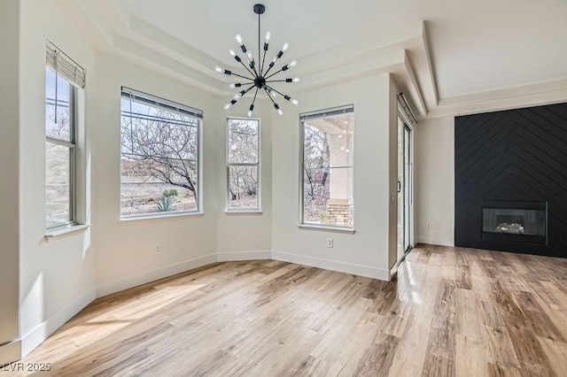 unfurnished dining area with a chandelier, a fireplace, baseboards, and wood finished floors