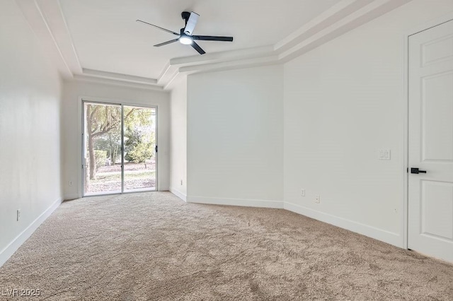 carpeted empty room featuring ceiling fan, a raised ceiling, and baseboards