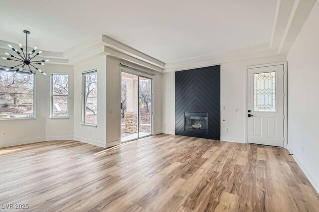 unfurnished living room featuring baseboards, a tray ceiling, a large fireplace, light wood-type flooring, and a chandelier