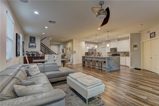 living room with a ceiling fan, visible vents, and wood finished floors