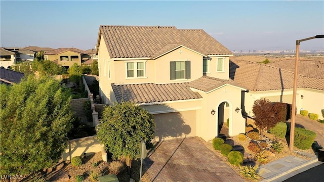 mediterranean / spanish house with decorative driveway, stucco siding, fence, a garage, and a tiled roof