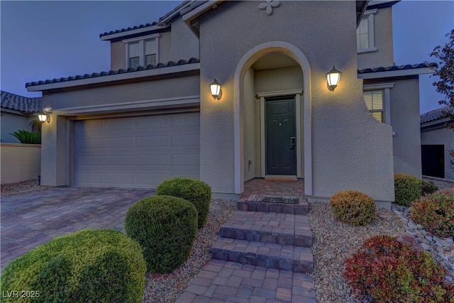 entrance to property with an attached garage, a tiled roof, decorative driveway, and stucco siding