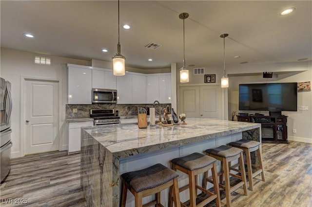 kitchen with tasteful backsplash, visible vents, white cabinets, wood finished floors, and stainless steel appliances