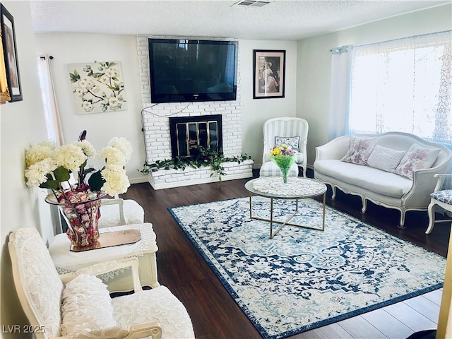 living area with a textured ceiling, a brick fireplace, wood finished floors, and visible vents