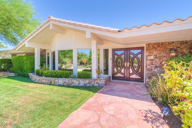 doorway to property featuring stone siding, a lawn, and a tiled roof