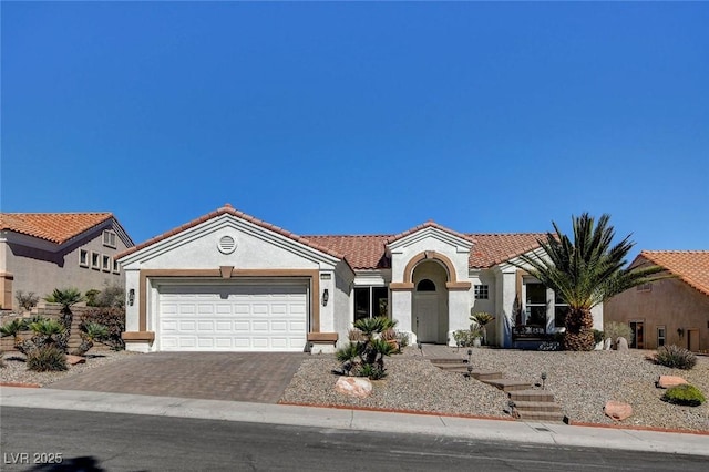 mediterranean / spanish-style house with an attached garage, a tiled roof, decorative driveway, and stucco siding