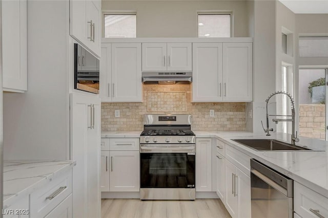 kitchen featuring light stone counters, under cabinet range hood, stainless steel appliances, a sink, and white cabinetry