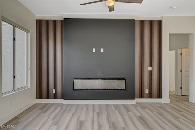 interior space featuring wood finished floors, a glass covered fireplace, a ceiling fan, and baseboards