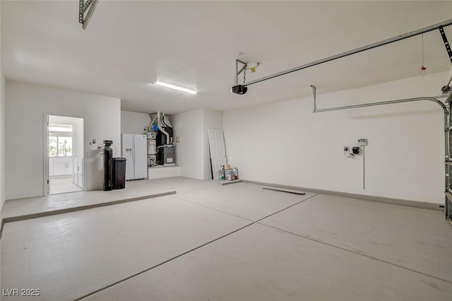 garage featuring heating unit, white fridge with ice dispenser, and a garage door opener