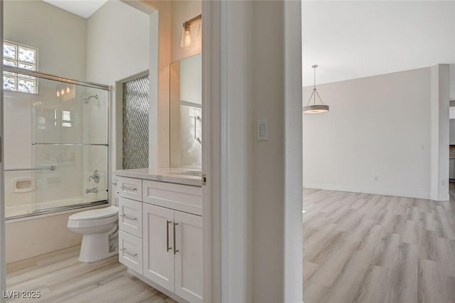 bathroom featuring enclosed tub / shower combo, toilet, wood finished floors, vanity, and baseboards