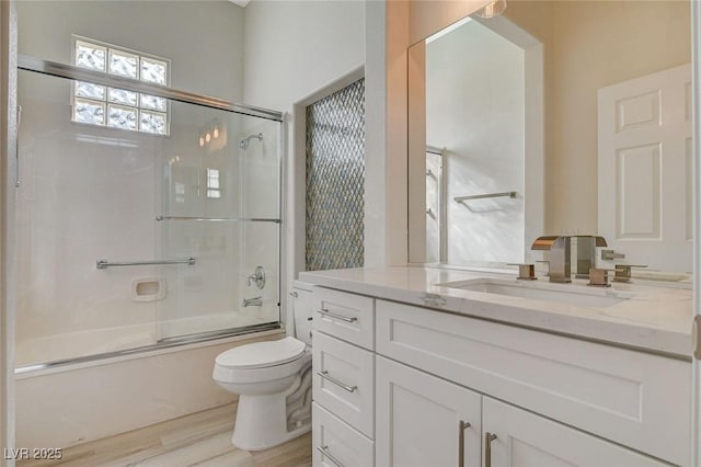 bathroom featuring enclosed tub / shower combo, vanity, wood finished floors, and toilet