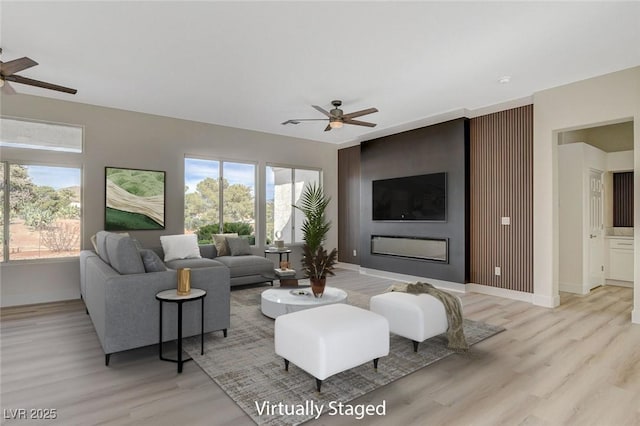 living area featuring ceiling fan, baseboards, and light wood-style flooring