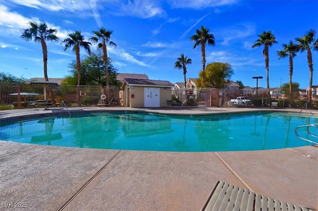 community pool with a patio area, fence, an outdoor structure, and a storage unit