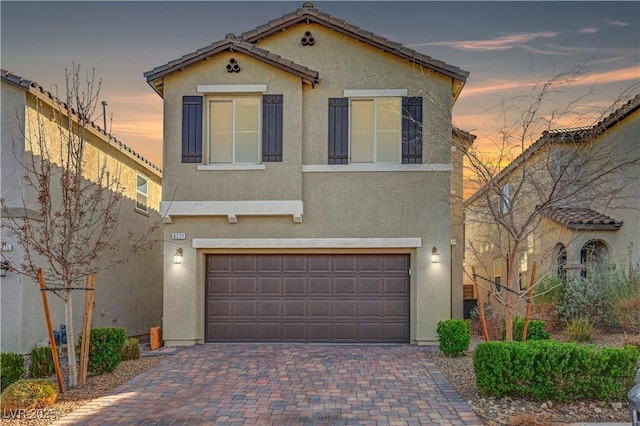 view of front facade with a garage, decorative driveway, a tile roof, and stucco siding