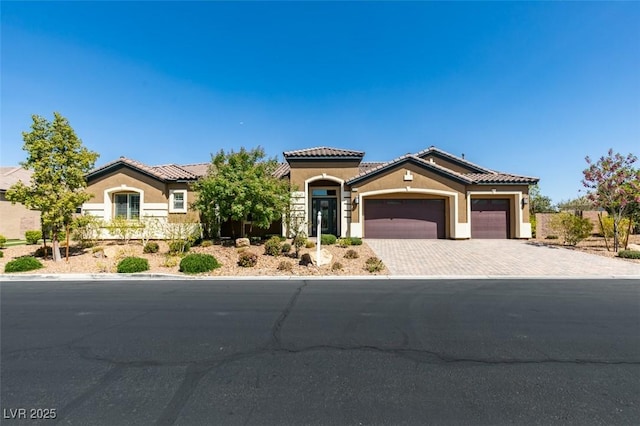 mediterranean / spanish-style house with decorative driveway, a tile roof, an attached garage, and stucco siding