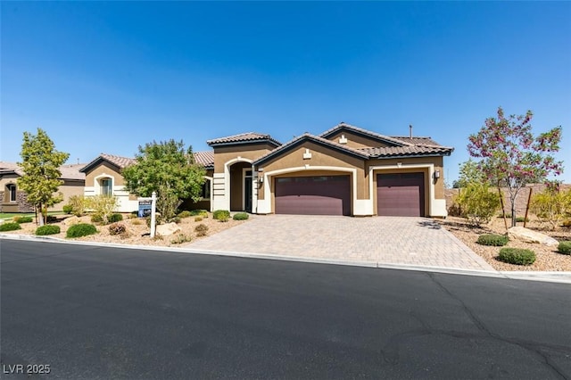 mediterranean / spanish-style home with decorative driveway, a tile roof, an attached garage, and stucco siding