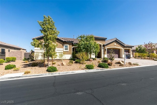 mediterranean / spanish home featuring a tile roof, stucco siding, fence, a garage, and driveway