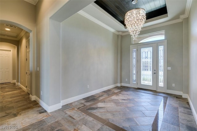 foyer with a tray ceiling, crown molding, arched walkways, and baseboards