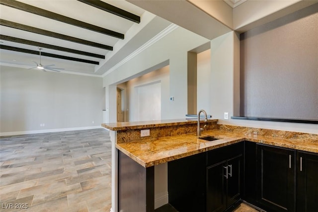 kitchen featuring light stone counters, a sink, dark cabinets, and beamed ceiling