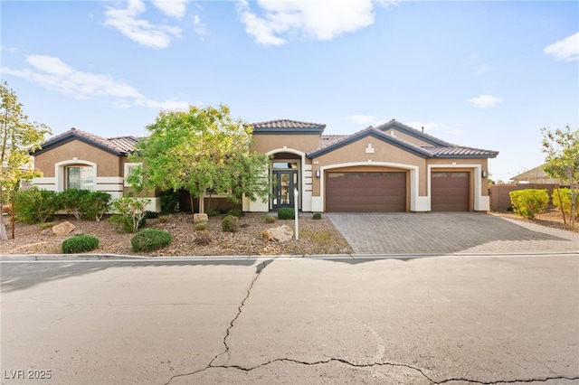 mediterranean / spanish-style house featuring stucco siding, an attached garage, a tiled roof, and decorative driveway