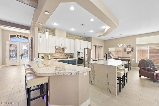 kitchen with a breakfast bar area, stainless steel appliances, decorative backsplash, a sink, and under cabinet range hood