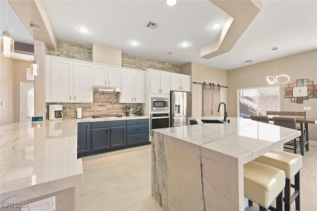 kitchen with visible vents, a sink, stainless steel appliances, a kitchen bar, and a barn door