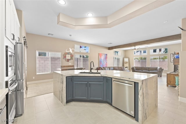 kitchen with light stone countertops, an island with sink, white cabinets, stainless steel appliances, and a sink