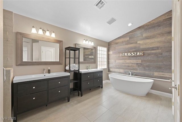 full bathroom with lofted ceiling, a freestanding tub, visible vents, and a sink